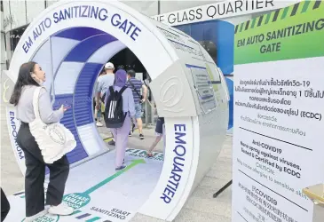  ??  ?? SAFE SHOPPING: Shoppers go through a tunnel designed to automatica­lly spray sanitising liquid as they walk into EmQuartier shopping complex in Bangkok. The gate uses nano technology.