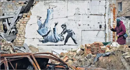  ?? AP ?? A woman takes a picture of artwork that might have been made by British street artist Banksy on a building destroyed by fighting in Borodyanka, in the Kyiv region.