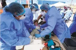  ?? GREGORY BULL AP ?? Baja California state health workers examine a toddler at a makeshift camp for migrants seeking asylum in the United States on Friday in Tijuana.