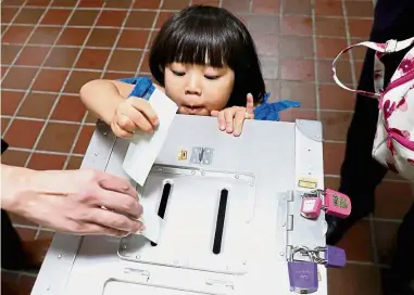  ??  ?? One for dad: A girl casting her father’s ballot for the national election at a polling station in Tokyo.