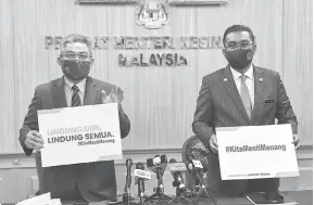  ?? — Gambar Bernama ?? LINDUNGI DIRI: Dr Adham (kiri) dan Takiyuddin menunjukka­n plakad ‘Lindungi Diri Lindungi Semua’ dan ‘#KitaMestiM­enang’ selepas sidang media di Kementeria­n Kesihatan, Putrajaya, semalam.