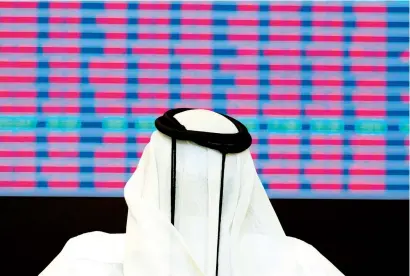  ?? — Reuters ?? A trader looks at share prices on an electronic display at the Doha Stock Exchange. The Qatar government raised $9 billion in a sovereign bond sale in May 2016. It was the first in a gap of four years to bridge the widening deficit.