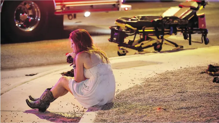  ?? JOHN LOCHER / THE ASSOCIATED PRESS ?? A woman sits on a curb after a mass shooting at a country music concert in Las Vegas on Sunday after a gunman opened fire on a crowd of more than 20,000 people, killing 59.