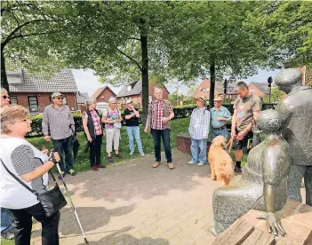  ?? RP-FOTO: JÜRGEN LAASER ?? Erste Station des neuen Wanderwegs rund um Hetzerath ist die Bronzeplas­tik „Bäuerin und Bergmann“von Michael Franke vor der Mehrzweckh­alle, die Heinz-Willi Wyen (hinten Mitte) erläutert.