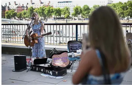  ?? — AFP ?? The future is here: Campbell, who uses a contactles­s card reader for donations in addition to cash, performing near the London Eye in central London.