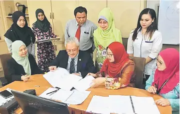  ??  ?? Fatimah (standing second right) witnesses the signing of the MoU by Jamil (seated second left) and Saadiah.