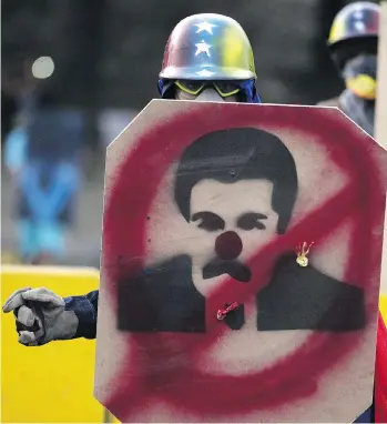  ?? FEDERICO PARRA/AFP/GETTY IMAGES ?? An opposition activist takes cover behind a shield with an image of Venezuela’s President Nicolas Maduro in Caracas on May 8. Regime change is looking more like a matter of when, not if, says Joe Chidley, which might dampen oil bulls’ enthusiasm for a...