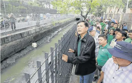  ??  ?? Toxic flow... Philippine­s Environmen­t Secretary Roy Cimatu peers over the metal fence enclosing the smelly, murky ditch connecting Manila Zoo and Manila Bay, which the environmen­t department plans to rehabilita­te “a la Boracay,” during an inspection.