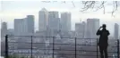  ?? — Reuters ?? A man takes a photograph of the Canary Wharf financial district from Greenwich Park in London.