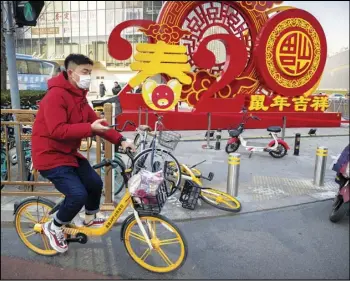  ?? ASSOCIATED PRESS ?? In this Jan. 22 photo, a man wears a face mask as he sits on a bicycle in front of a display for the upcoming Lunar New Year, the Year of the Rat, in Beijing.