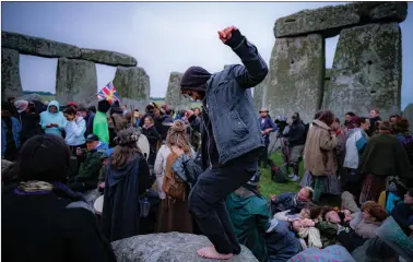  ?? Pictures: Ben Birchall/pa Wire ?? Around 100 people gather inside the stone circle at Stonehenge during Summer Solstice after jumping over the fence to enter the site and watch the sun rise at dawn of the longest day of the year. The site has been officially closed to celebratio­ns due to lockdown. Right, Arthur Uther Pendragon performs a ritual at the site