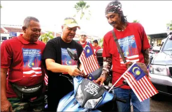  ??  ?? Amiruddin Hamzah (centre) installs Jalur Gemilang on one of the participan­ts’ motorcycle. — Bernama photo