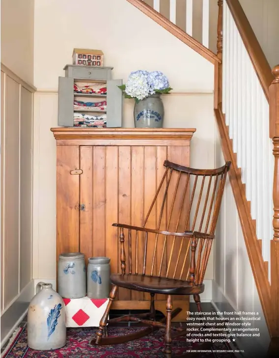  ??  ?? The staircase in the front hall frames a cozy nook that houses an ecclesiast­ical vestment chest and Windsor-style rocker. Complement­ary arrangemen­ts of crocks and textiles give balance and height to the grouping.