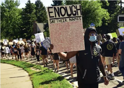  ?? Jeremy Papasso, Daily Camera ?? Colorado defensive back Chris Miller holds a sign as protesters pass by during a Black Lives Matter march on Friday in Boulder. The march was in response to the recent killing of George Floyd by a white police officer.