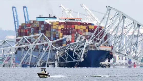  ?? MARK SCHIEFELBE­IN/AP ?? A boat moves past a container ship as it rests against wreckage of the Francis Scott Key Bridge on Tuesday as seen from Pasadena, Maryland. The container ship lost power and rammed into the major bridge in Baltimore early Tuesday, causing it to snap and plunge into the river below.