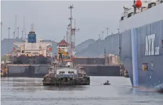  ?? JUSTIN SULLIVAN/GETTY IMAGES/TNS ?? Dock workers on a row boat pull a rope between the dock and the vehicle carrier Sirius Leader on Sept. 23 as it prepares to enter the Miraflores locks while transiting the Panama Canal.