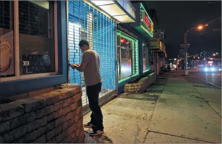  ?? SETH WENIG — THE ASSOCIATED PRESS ?? On a mostly empty street, an employee of Justin’s BBQ closes up for the night Nov. 12 in Newark, N.J.