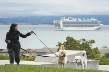  ?? Paul Kuroda / Special to The Chronicle ?? Helen Aumann walks her dogs Ghostbuste­r and Hazel (right) with the Grand Princess anchored off Hunters Point in S.F.