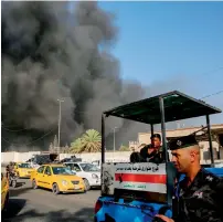  ?? AFP ?? Members of the Iraqi federal police stand outside the country’s biggest ballot warehouse, where votes for the eastern Baghdad district were stored, as a column of black smoke billows from the building, in Baghdad. —