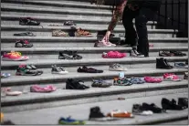  ?? CP PHOTO DARRYL DYCK ?? A woman places one of 215 pairs of children’s shoes on the steps of the Vancouver Art Gallery as a memorial to the 215 children whose remains are believed to have been found buried at the site of a former residentia­l school in Kamloops, in Vancouver, on Friday, May 28, 2021.