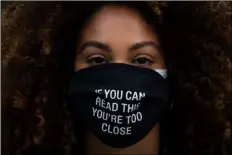  ?? AP FILE PHOTO/JAE C. HONG ?? In this Monday file photo, Daisha Graf, 34, pauses for photos wearing a face mask with a message that reads “If you can read this, you’re too close,” in Los Angeles.