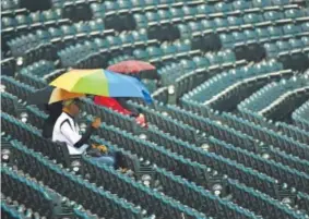  ??  ?? Rockies fans take cover as the grounds crew covers the field during rain before the game against the Washington Nationals on Tuesday night at Coors Field. The game was delayed 1 hours, 16 minutes. John Leyba, The Denver Post