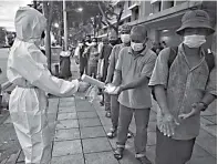  ?? LILLIAN SUWANRUMPH­A/AFP ?? TERTIB: Seorang relawan yang mengenakan APD menyemprot­kan cairan pembersih tangan kepada para tunawisma dan penduduk berpenghas­ilan rendah yang mengantre untuk menerima bantuan makanan di dekat Monumen Demokrasi, Bangkok, Jumat (16/7).