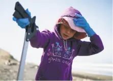  ??  ?? Grace Coachman, 6, holds down her hat as she picks up trash on the windy beach during the annual event.