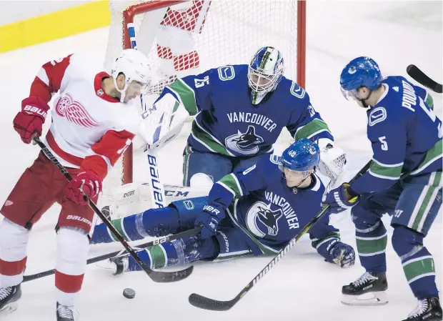  ?? — CP ?? Vancouver Canucks centre Elias Pettersson, sliding, and defenceman Derrick Pouliot, right, help stop Detroit Red Wings centre Andreas Athanasiou from getting a shot on Canucks goaltender Jacob Markstrom during second period NHL action in Vancouver on Sunday.
