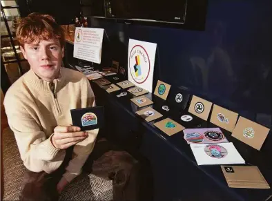  ?? Christian Abraham / Hearst Connecticu­t Media ?? Sixteen-year-old Bobby Callagy poses with some of the products he sells in his home in Darien. Callagy started his own company, called Make Change, selling wallets, stickers and patches. A portion of the proceeds go to support organizati­ons such as Greenpeace and The Trevor Project.