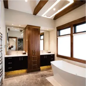  ??  ?? Marble tile is warmed with hydronic heat that spreads to a white inlay that borders the freestandi­ng bath. Walnut clad beams match tower features that centre a dual, floating vanity of rift-cut white oak surfaced in quartz.