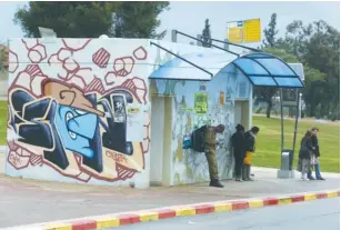  ?? (Marc Israel Sellem/The Jerusalem Post) ?? PEOPLE WAIT for a bus in Sderot yesterday, next to a rocket shelter.