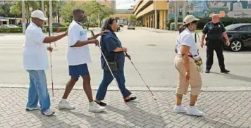  ?? AMY BETH BENNETT/SOUTH FLORIDA SUN SENTINEL ?? Blind pedestrian­s cross a Fort Lauderdale street at a 2019 White Cane Safety Day walk. Two Florida high school students have updated the white cane to add digital improvemen­ts.