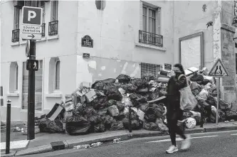  ?? Aurelien Morissard/associated Press ?? A woman covering her nose walks past uncollecte­d garbage in Paris on Monday. Sanitation workers have been on strike since March 6, upset by France’s attempts at pension reform.