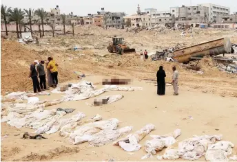  ?? — AFP photo ?? People gathering near bodies lined up for identifica­tion after they were unearthed from a mass grave found in the Nasser Medical Complex in the southern Gaza Strip.