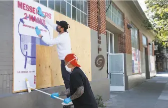  ?? Photos by Paul Chinn / The Chronicle ?? Eric Bailey (top) and Nelson Garcia post a billboard outside the S.F. factory Timbuk2 reopened.