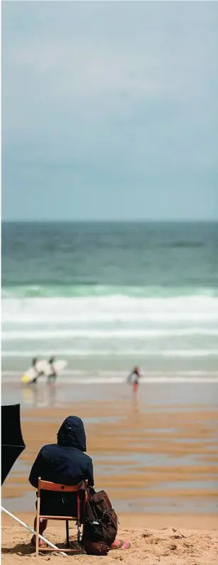  ?? EFE ?? Un joven sentado junto a una sombrilla contempla ayer a unos practicant­es de surf en una casi desierta playa de Zurriola en San Sebastián