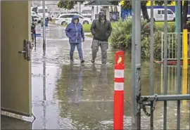  ?? Irfan Khan Los Angeles Times ?? TWO VOTERS walk through ankle-deep rainwater to reach a polling station at Ruben Salazar Park in East Los Angeles on Tuesday.