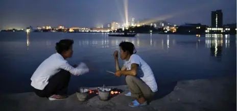  ?? WONG MAYE-E PHOTOS/THE ASSOCIATED PRESS ?? North Korean women talk over pots of burning charcoal used for cooking seafood on a pier in Wonsan, North Korea.