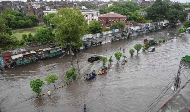  ?? Agence France-presse ?? ↑
Commuters make their way through a flooded street after heavy monsoon rain in Lahore on Tuesday.