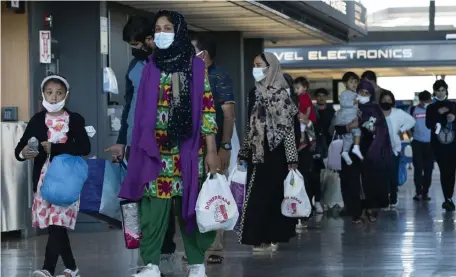  ?? Ap pHOTOS ?? GOING SOMEWHERE? Families evacuated from Afghanista­n, above and far right, walk through the terminal Friday at Dulles Internatio­nal Airport in Chantilly, Va., before boarding a bus. Massachuse­tts has put out the ‘welcome’ sign, but details about receiving evacuees have been slow to emerge from the Biden administra­tion.