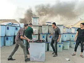  ?? [AP FILE PHOTO] ?? Iraqi electoral officials work to salvage ballot boxes as smoke rises from a fire that broke out at Baghdad’s largest ballot box storage site, where ballots from Iraq’s May parliament­ary elections are stored, June 10 in Baghdad, Iraq.