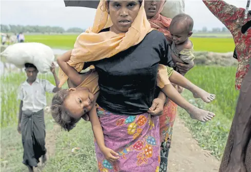  ?? AFP ?? A Rohingya Muslim refugee carries a child as they arrive from Myanmar through Lomba Beel after crossing the Naf River, in the Bangladesh­i town of Teknaf yesterday.