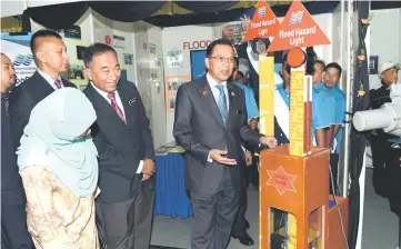  ??  ?? Hamim (right) taking a closer look at a flood hazard light after launching the DID’s 2017 Innovation Day celebratio­n ceremony. — Bernama photo