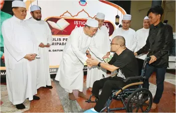  ?? — Bernama photo ?? Hajiji presenting contributi­on to asnaf during the Nuzul Al-Quran celebratio­n at the State Mosque.