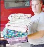  ?? TIMES photograph by Annette Beard ?? Showing off some of the quilts donated by Stitched With Love is firefighte­r Quinn Gehler.