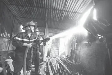  ?? — AFP photo ?? A firefighte­r uses a hose to douse a spot while battling a fire in a workshop complex in Hanoi.