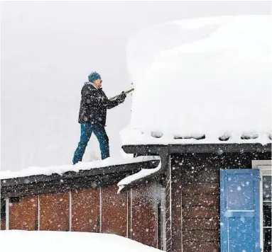  ??  ?? Ein Mann schaufelt den meterhohen Schnee von einem Hausdach in Davos. Denn der Schnee wurde immer