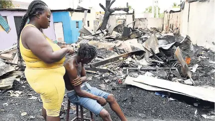  ?? RICARDO MAKYN PHOTOS ?? Kaysia Williams does Delano Wright’s hair even as he sits among the remnants of his home, which was one of those burnt out in Denham Town on Sunday.