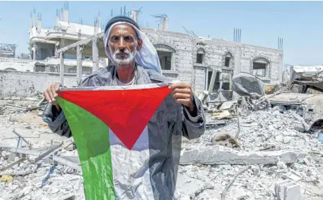  ?? FOTO: IMAGO ?? Ein Mann steht mit einer palästinen­sischen Flagge inmitten der Trümmer eines zerstörten Hauses im Gazastreif­en. Tolerantes und friedliche­s Zusammenle­ben zwischen Israelis und Arabern sieht anders aus.